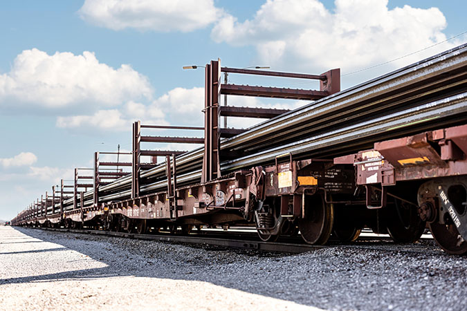Finished continuous welded rail sticks being loaded onto specialized flat car racks for final transport Finished continuous welded rail sticks being loaded onto specialized flat car racks for final transport